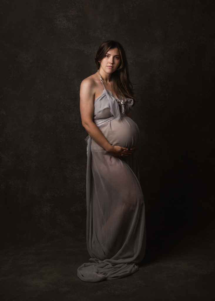 Pregnant woman wearing custom grey sheer gown with crystal and leather necklace for maternity photo shoot