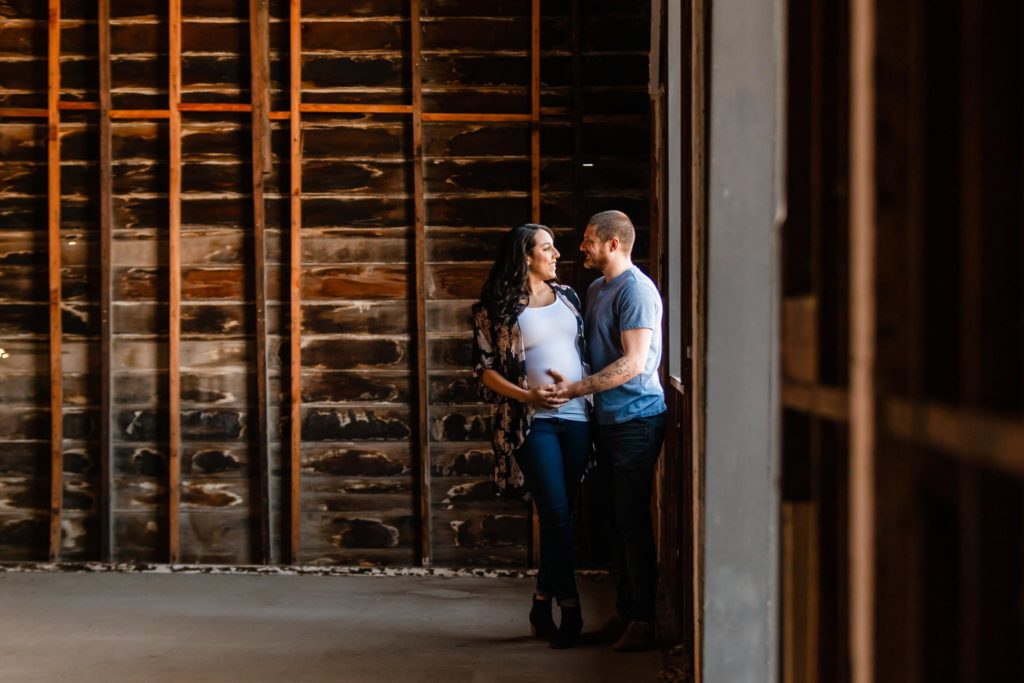 Casual photo of couple looking at each other and embracing while wearing casual clothing for couples maternity shoot at San Francisco Bay Area photo studio