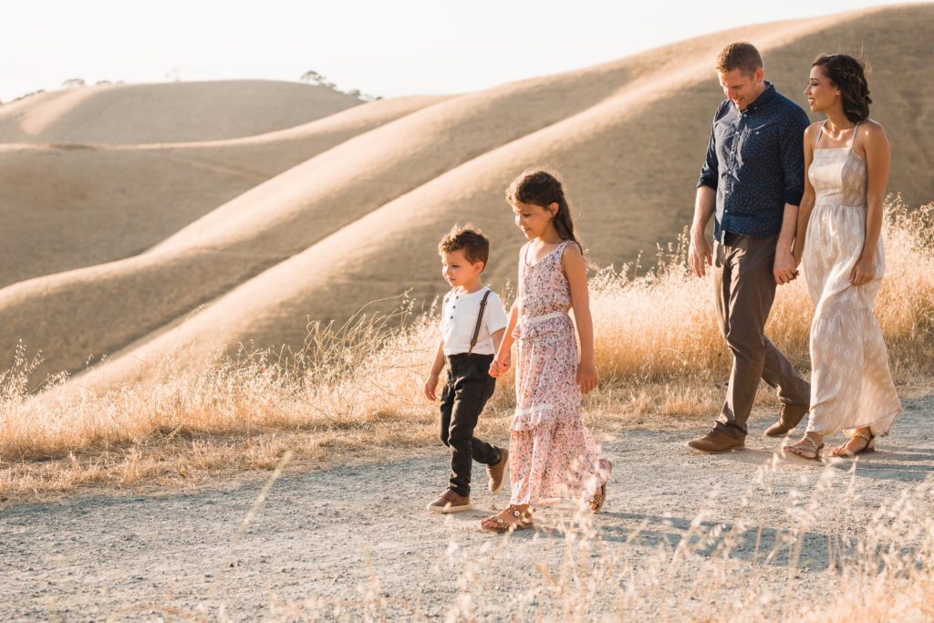 Mother and father walk behind their son and daughter in the Livermore East Bay hills during family sunset photo session