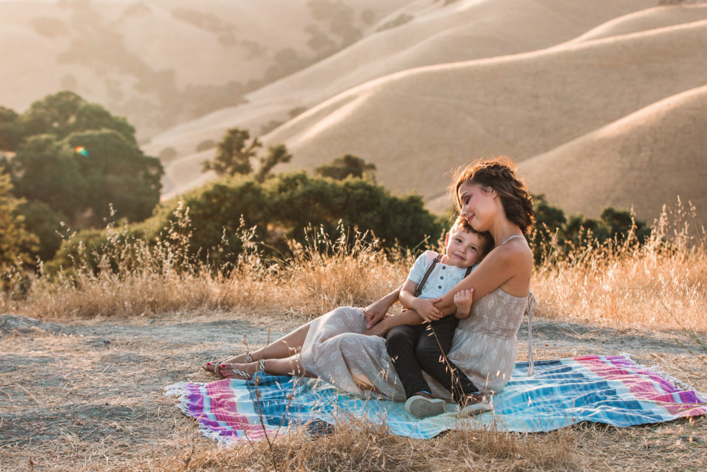 Mother holds son on her lap as he looks at camera during sunset photo session