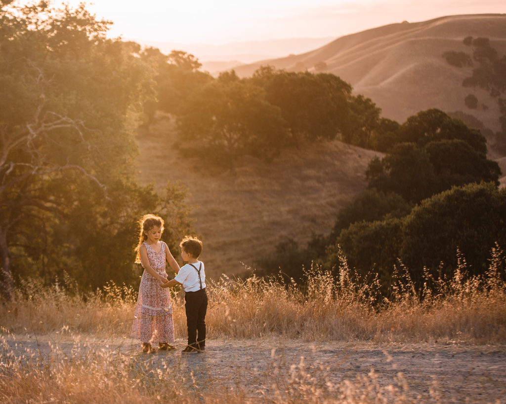Brother and sister children hold hands at Golden hour with California hills in the background