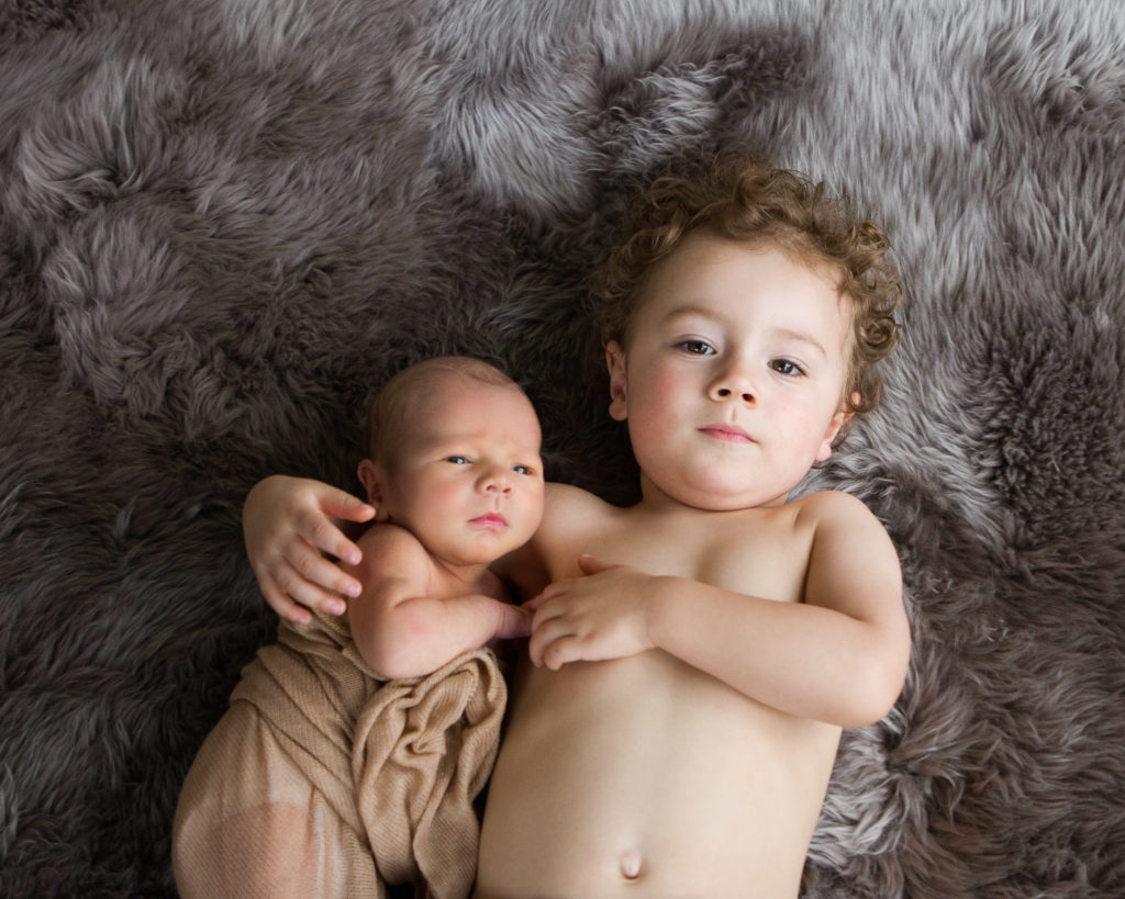 Newborn photo session with baby boy being held by big brother who is not wearing a shirt.