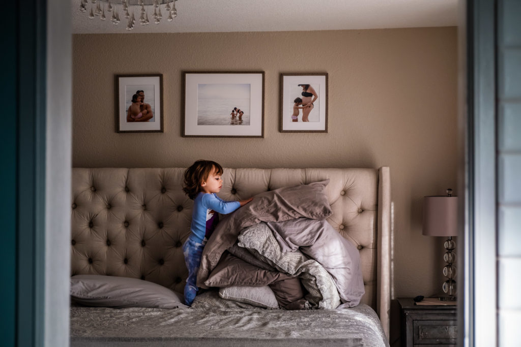 Toddler girl piling pillows on parents bed in an attempt to help make the bed