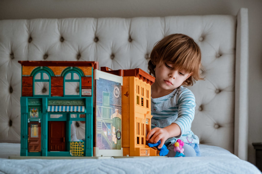 Toddler girl plays with vintage Sesame Street toy house on parents bed.